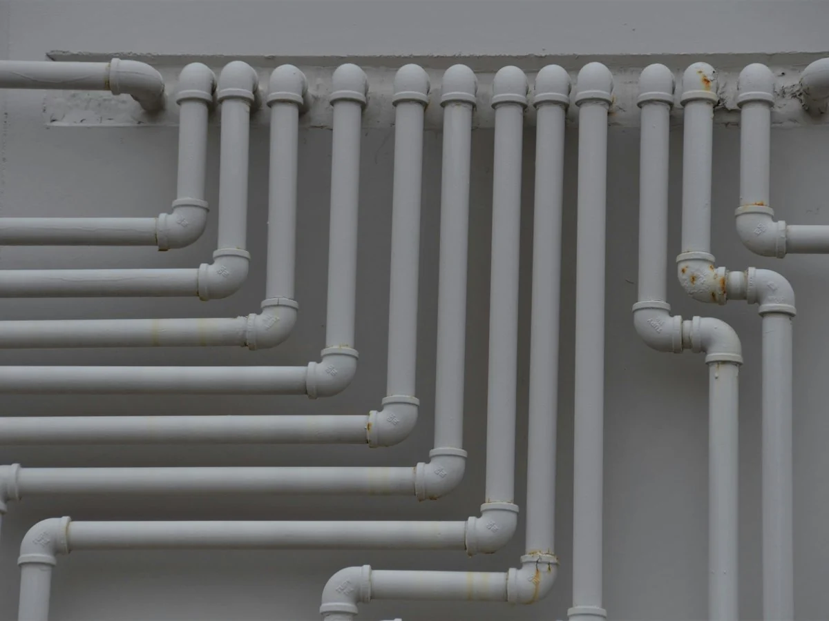 Neat rows of grey pipework on a building wall, every run in its place, like job documents filed on the job they belong to
